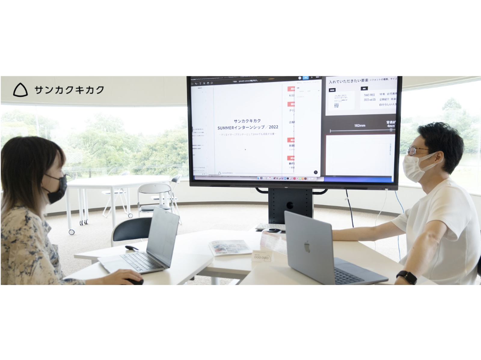 「SUMMERインターンシップ／2022」の資料を映した大型モニターを前に、ノートパソコンを開いて打ち合わせる男女