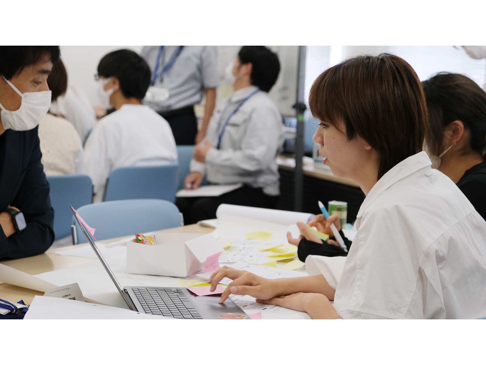 付箋を広げた机でノートパソコンを操作しながら話し合う学生たち