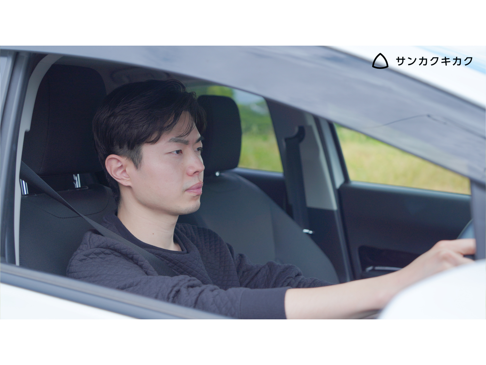 白い車の運転席でハンドルを握る男性