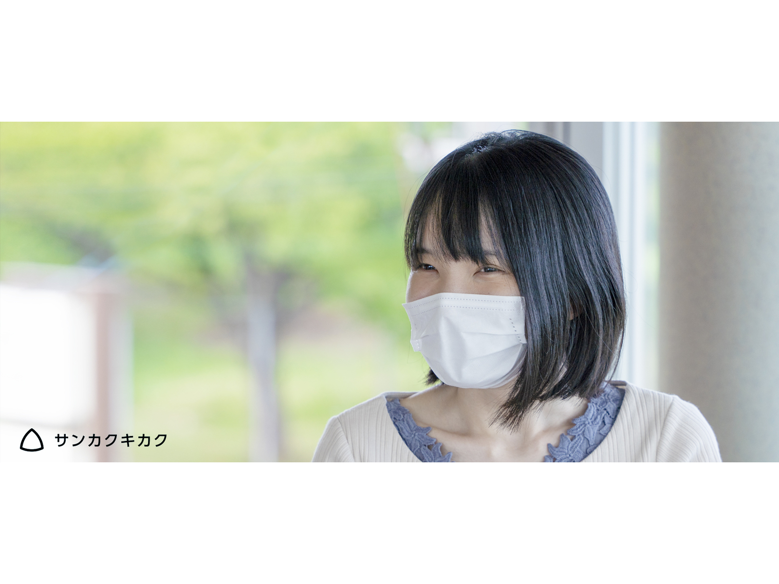 緑の見える窓辺で、笑顔で話を聞くマスク姿の女性