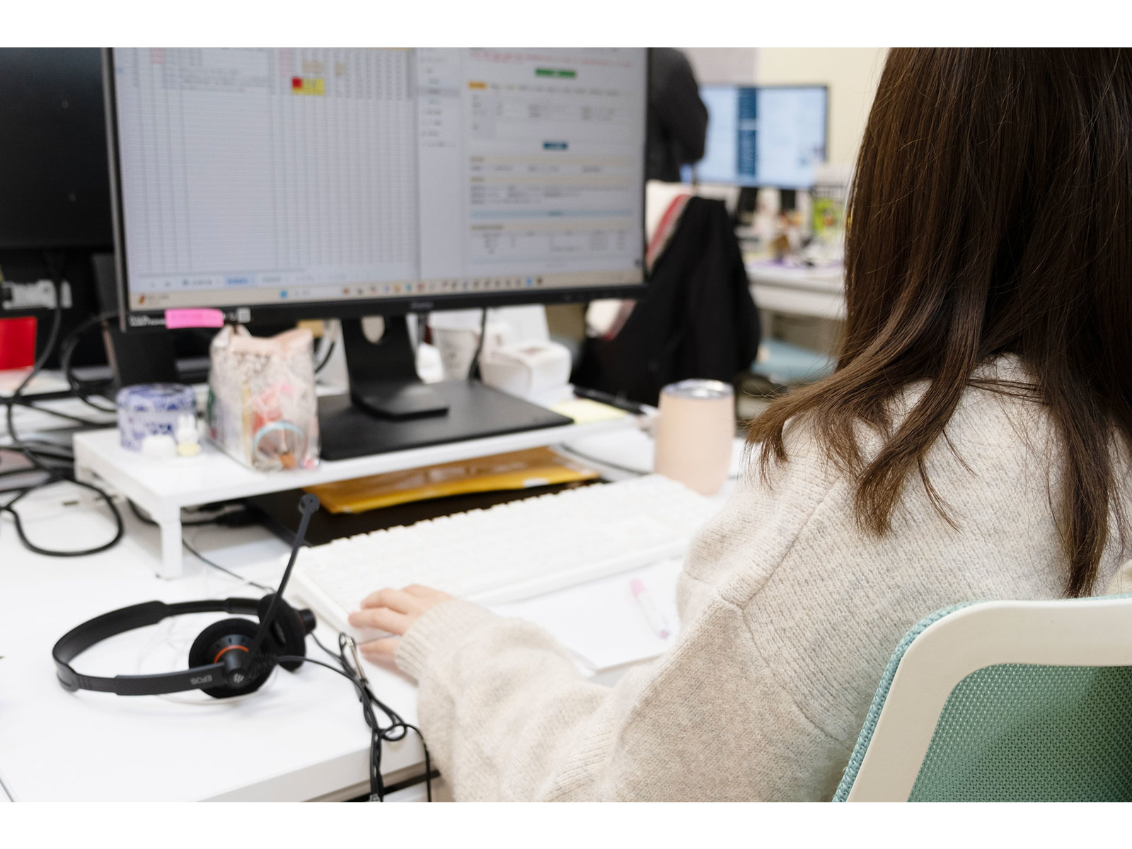 表計算の画面を映したモニターに向かい、ヘッドセットを横に置いてキーボードを打つ女性