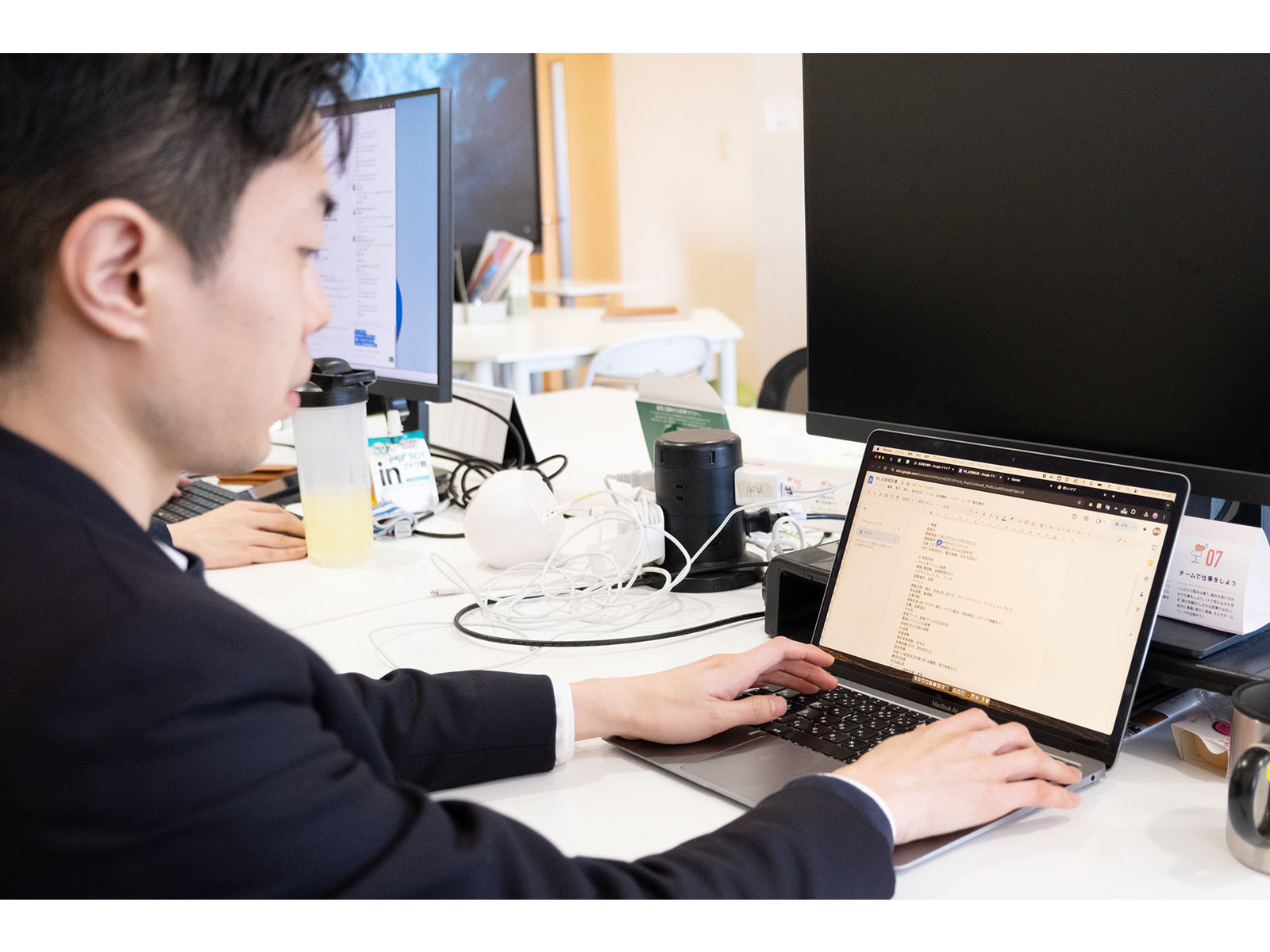 文書を開いたノートパソコンでキーボードを打つ、ジャケット姿の男性