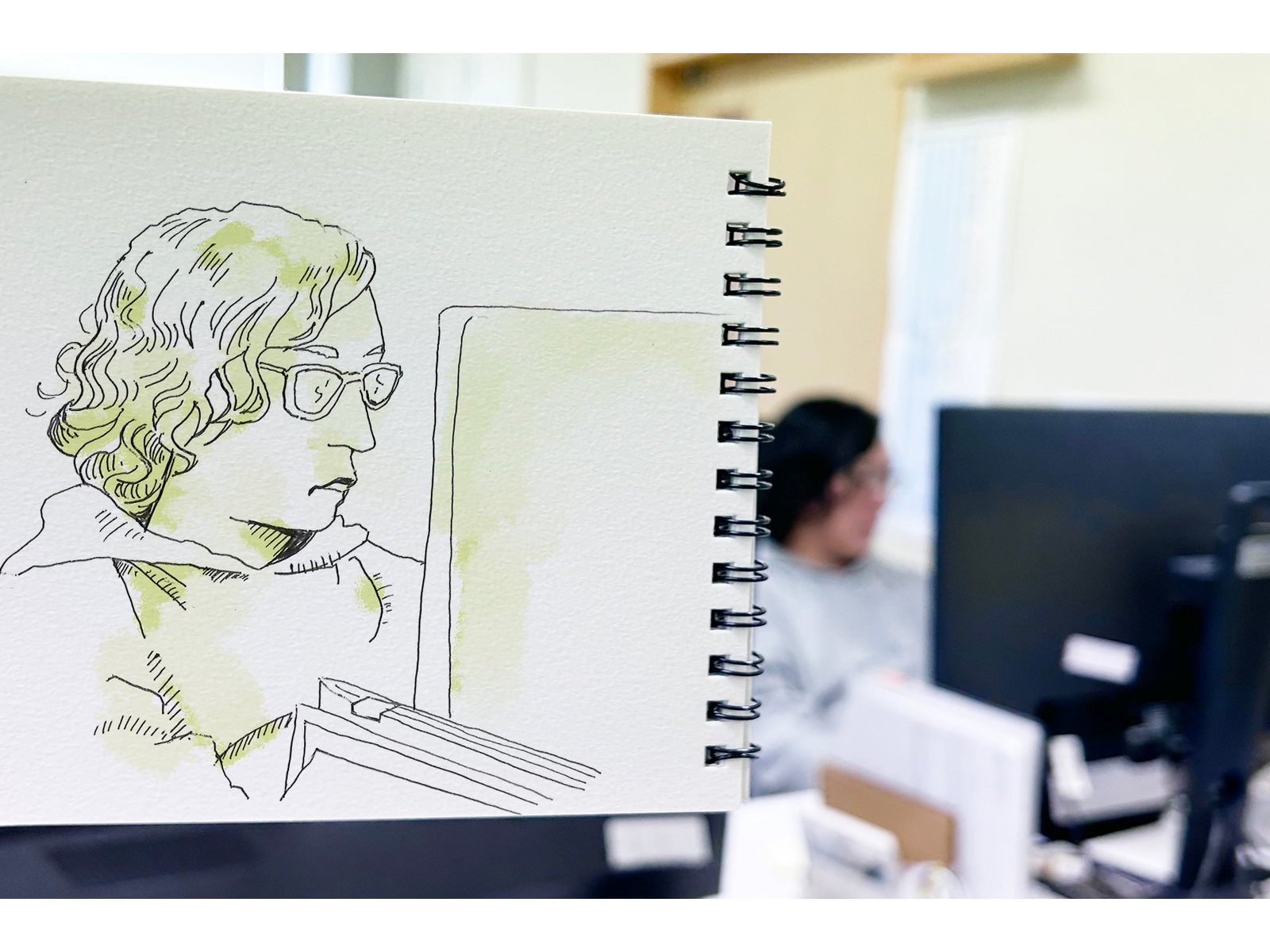 モニターに向かう人を背景に、眼鏡をかけてパソコンを見つめる人を描いた淡い緑のペン画スケッチ