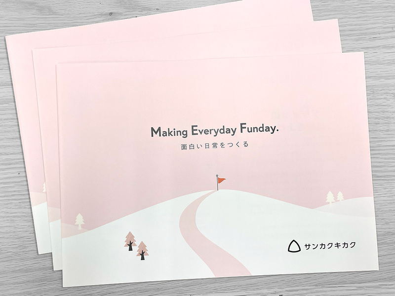 淡いピンクの丘と旗のイラストに「Making Everyday Funday. 面白い日常をつくる」と書かれた横長のパンフレットの表紙3部