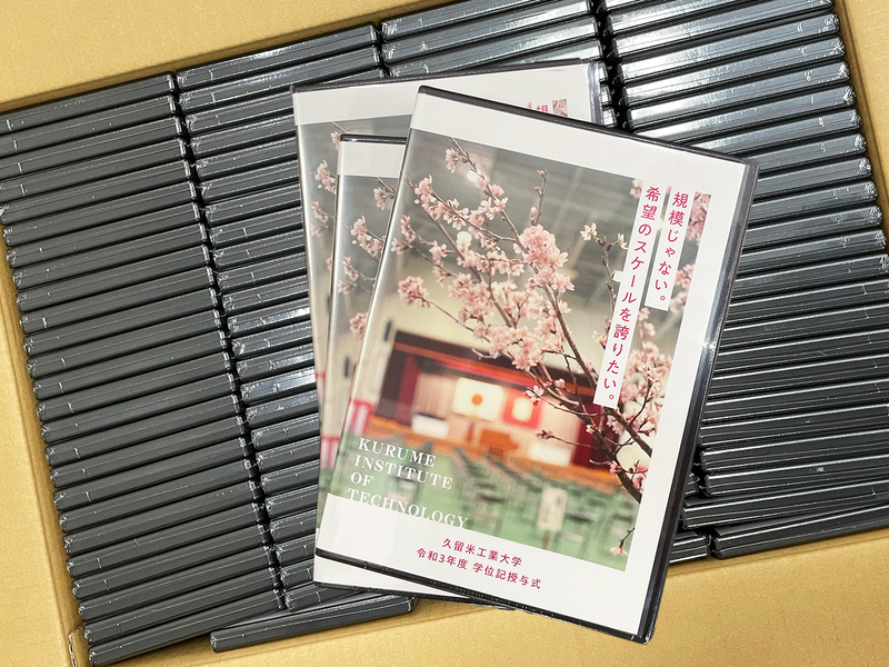 段ボール箱に詰めたディスクケースの上に、桜の枝と式場の写真に「規模じゃない。希望のスケールを誇りたい。」と書かれたケースを数枚重ねたもの